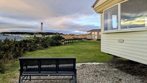 A bench in a grassy area with a view of a lighthouse in the distance.