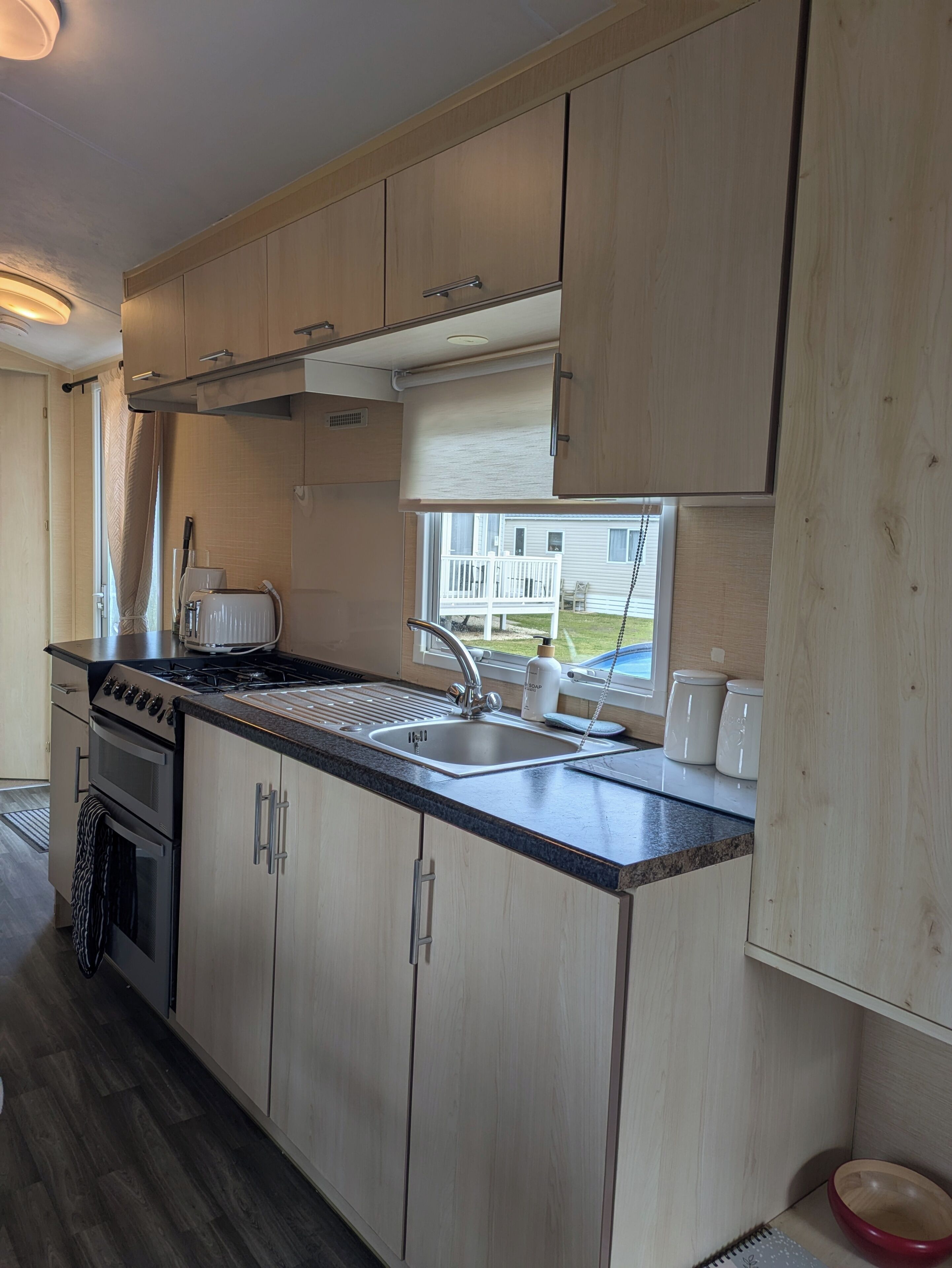 Une cuisine moderne avec des meubles en bois, une cuisinière à gaz, un évier et une fenêtre donnant sur l’extérieur.