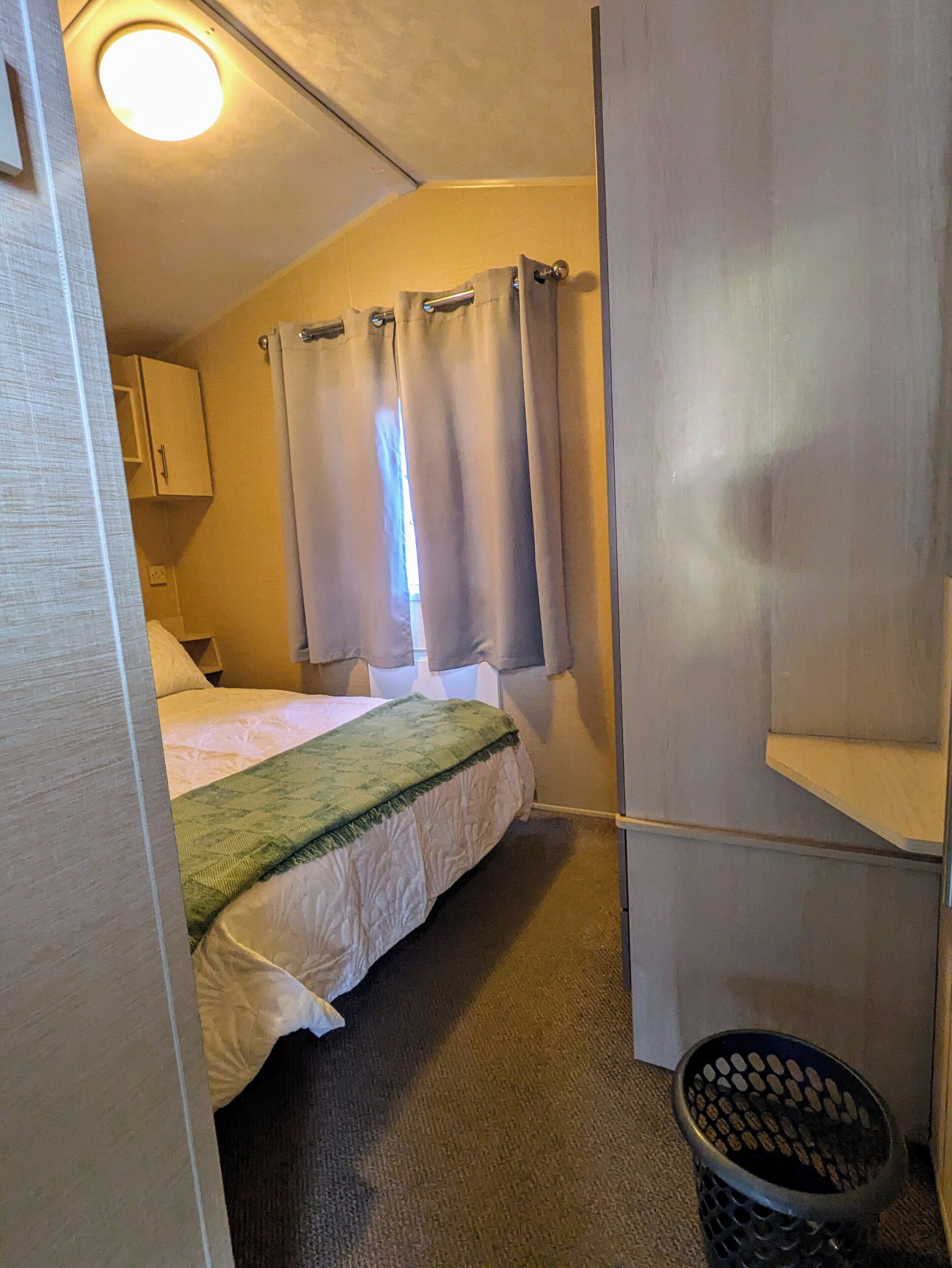 Ein kleines, gemütliches Schlafzimmer mit Bett, Nachttisch, Schrank und einem Fenster mit Vorhängen.