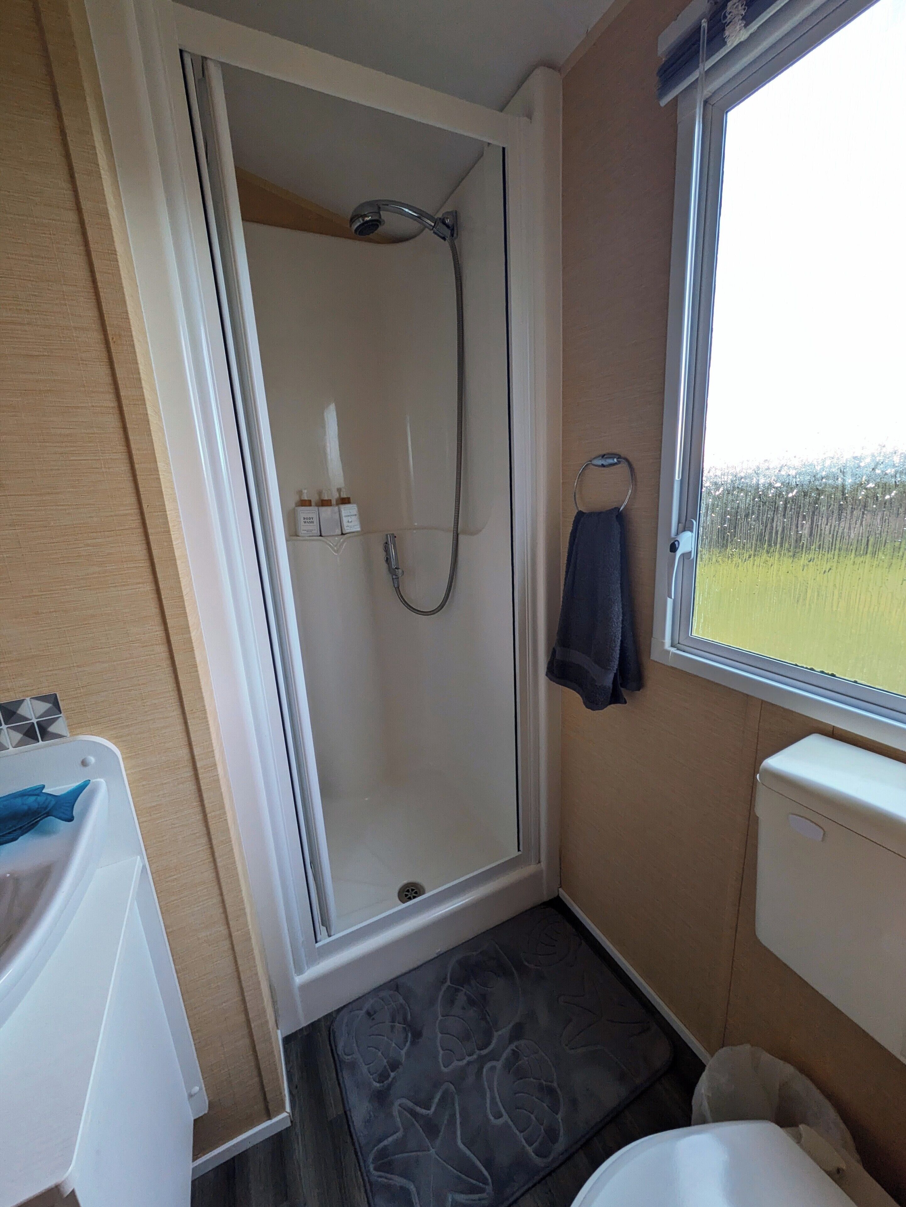 A bathroom with a glass shower door, a toilet, a sink, and a window with a view of greenery.