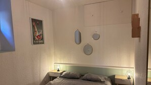 A bedroom with a bed, two bedside tables, a poster on the wall, and three wall-mounted mirrors.