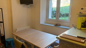 A small kitchen with a table, chairs, a window with a view, a TV mounted on the wall, and a coffee maker.