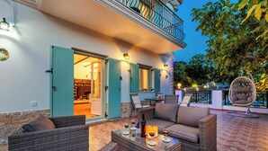 An outdoor seating area with wicker furniture, a glass-top table with wine glasses, and a balcony with a hanging chair. - Villa Augusta - Two Bedroom Villa, Sleeps 4 (Sporades)