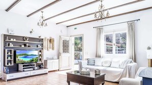 A spacious living room with a large flat-screen TV, a sofa, a coffee table, and a TV stand with shelves. - Villa Augusta - Two Bedroom Villa, Sleeps 4 (Sporades)
