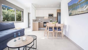 A modern living space with a sofa, a dining table, and chairs. There is a kitchen area with cabinets and a microwave. A painting is on the wall. - Villa Averto Anna - Two Bedroom Villa, Sleeps 4 (Rachi)