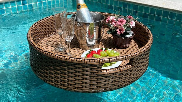 A poolside setting with a wicker basket containing a bottle of champagne, glasses, strawberries, grapes, and a flower arrangement. - CHALÉS PRINCESA ISABEL (Petrópolis)