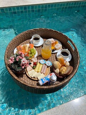 A wicker tray with breakfast items including fruits, pastries, and beverages by a pool. - CHALÉS PRINCESA ISABEL (Petrópolis)