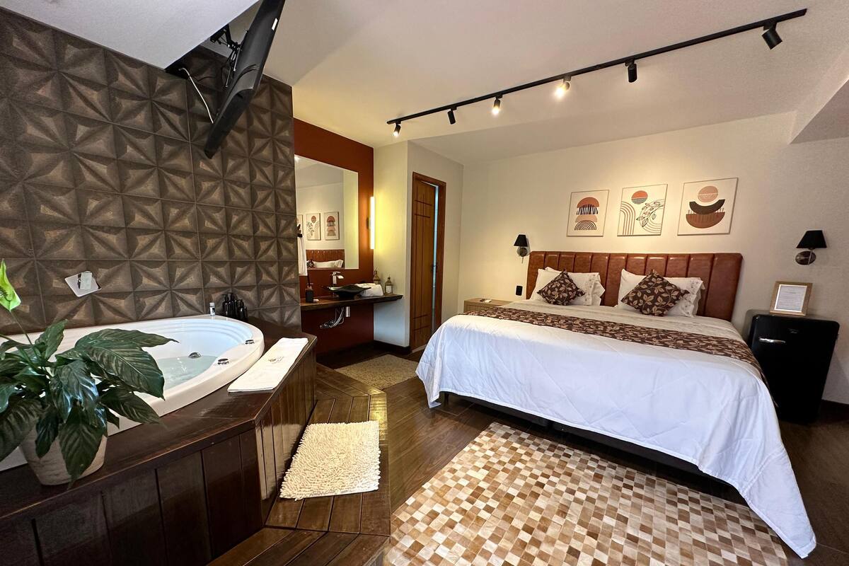 Une chambre d’hôtel moderne avec un grand lit, une salle de bain séparée avec une baignoire, un plancher en bois et un tapis à carreaux.