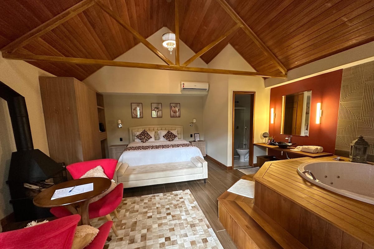 Une chambre à coucher avec un grand lit, un plafond en bois, un lustre, un fauteuil rouge, une coiffeuse en bois et une baignoire.