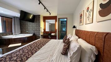 A hotel room with a large bed, a bathroom with a bathtub, and a TV mounted on the wall.
