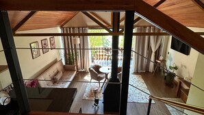 A spacious living area with a high ceiling and a chandelier, a sofa, a coffee table, and a view of the outdoors. - CHALÉS PRINCESA ISABEL (Petrópolis)