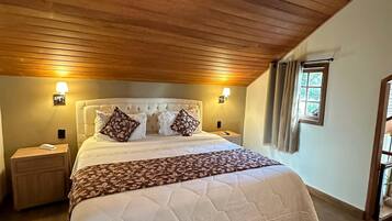 Un dormitorio con techo de madera, una cama grande con edredón blanco acolchado, almohadas estampadas y dos lámparas de noche.