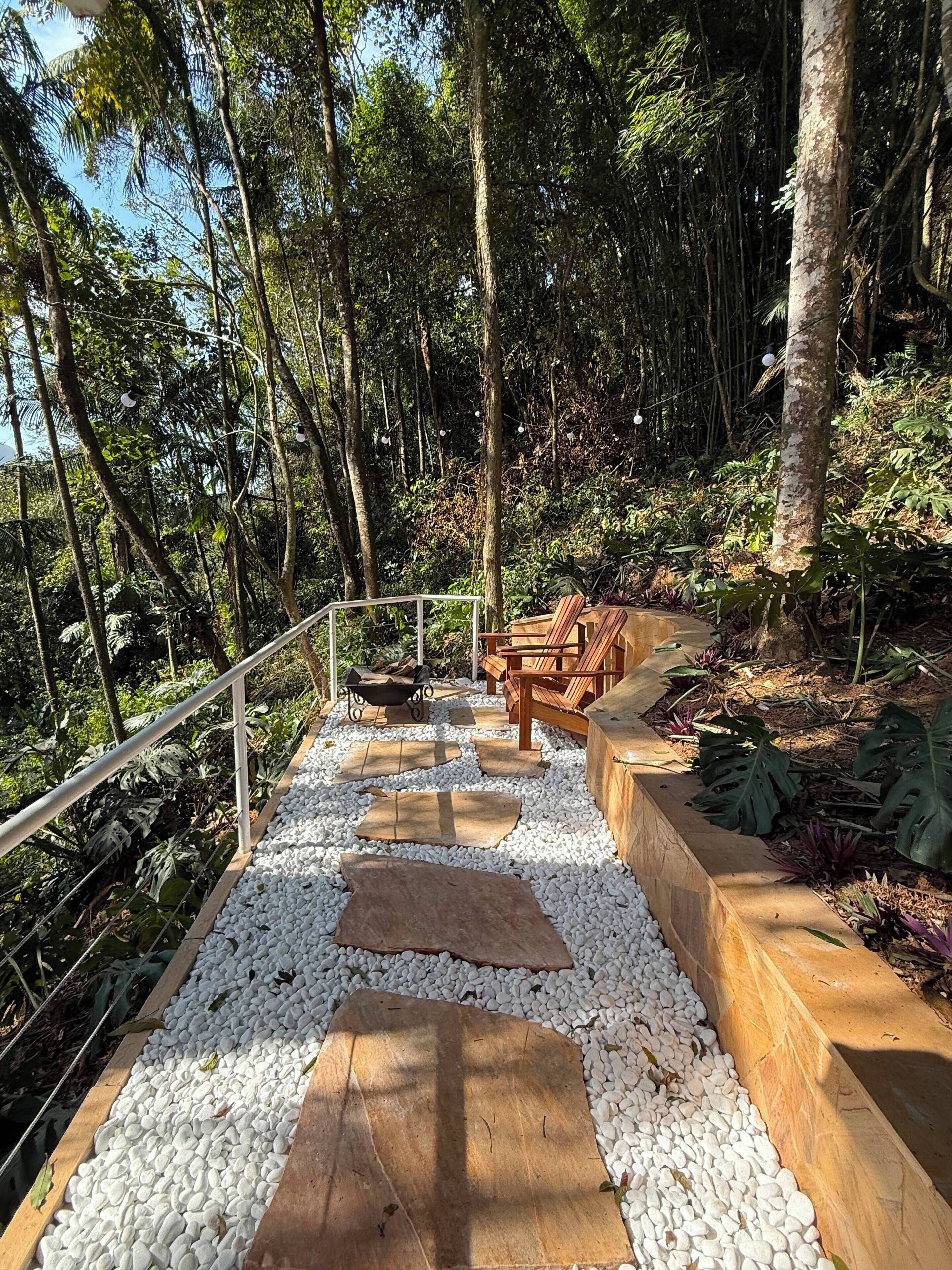 Um caminho com pedras brancas e tábuas de madeira, ladeado por vegetação exuberante e árvores.