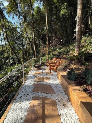 A pathway with white pebbles and wooden planks, surrounded by lush greenery and trees. - CHALÉS PRINCESA ISABEL (Petrópolis)