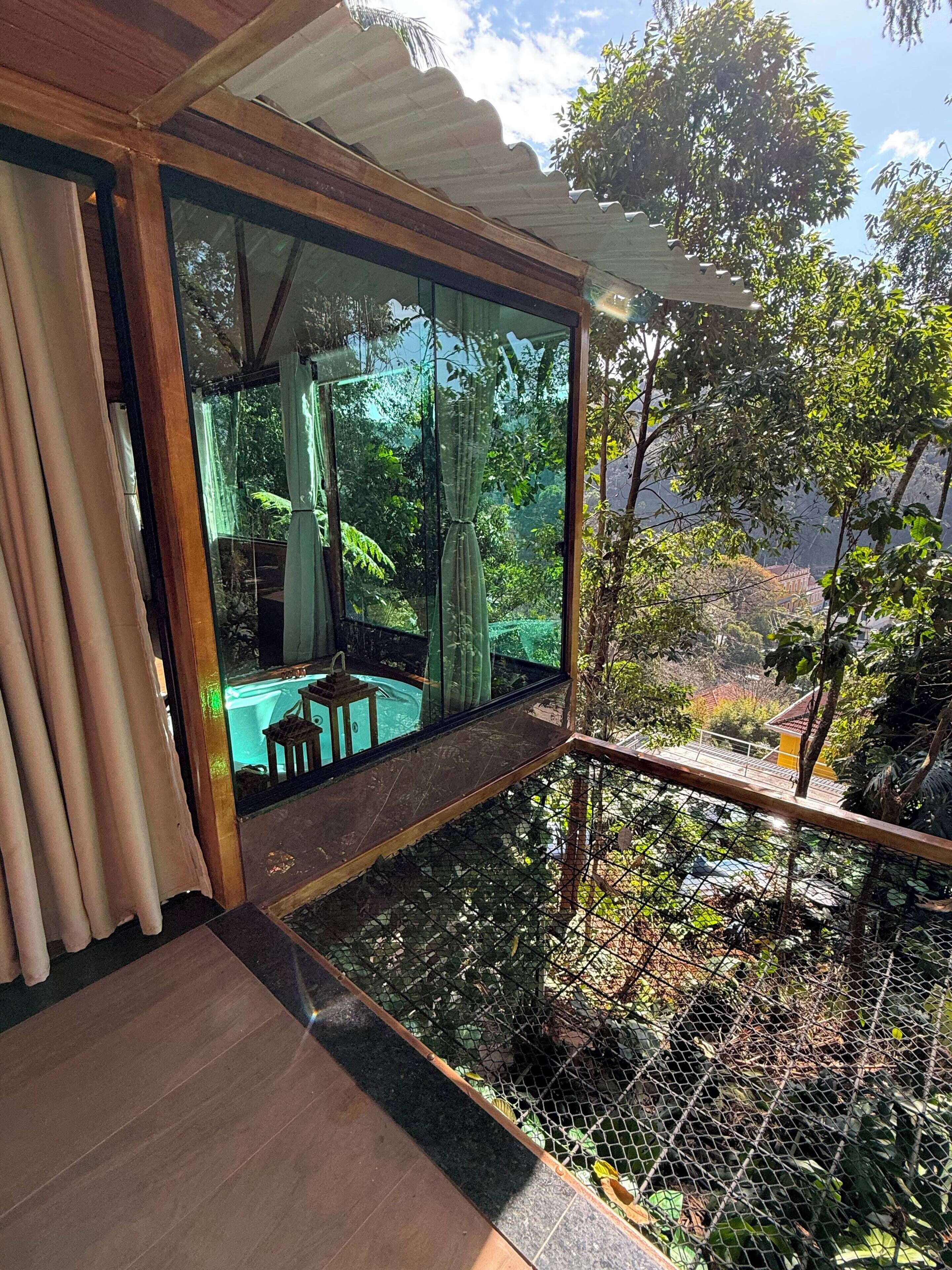 Ein Zimmer mit Glaswand, Holzboden und Blick auf Garten sowie eine Sitzgelegenheit im Freien.