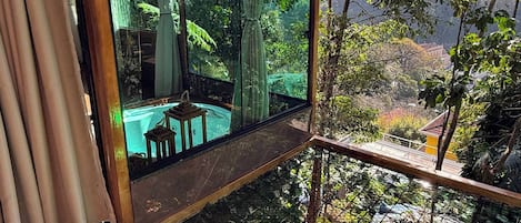 Una habitación con pared de vidrio, suelo de madera y vistas a un jardín y zona de estar exterior.