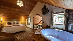 A bedroom with a large bed, a wooden ceiling, a TV mounted on the wall, and a window with curtains. - CHALÉS PRINCESA ISABEL (Petrópolis)