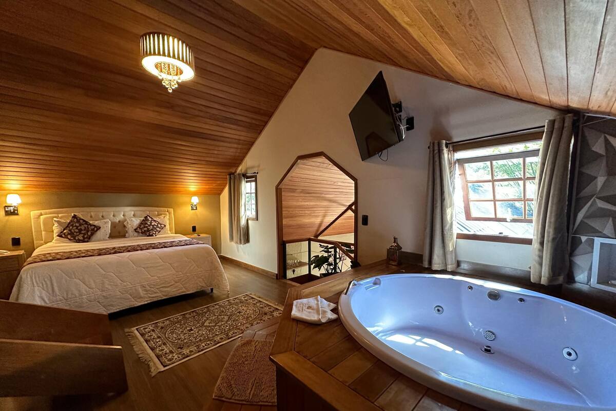 Une chambre à coucher avec un grand lit, un plafond en bois, un téléviseur fixé au mur et une fenêtre avec des rideaux.