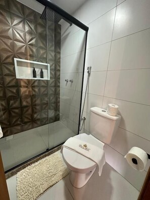A modern bathroom with a glass shower enclosure, a toilet, and a shelf with toiletries. - CHALÉS PRINCESA ISABEL (Petrópolis)