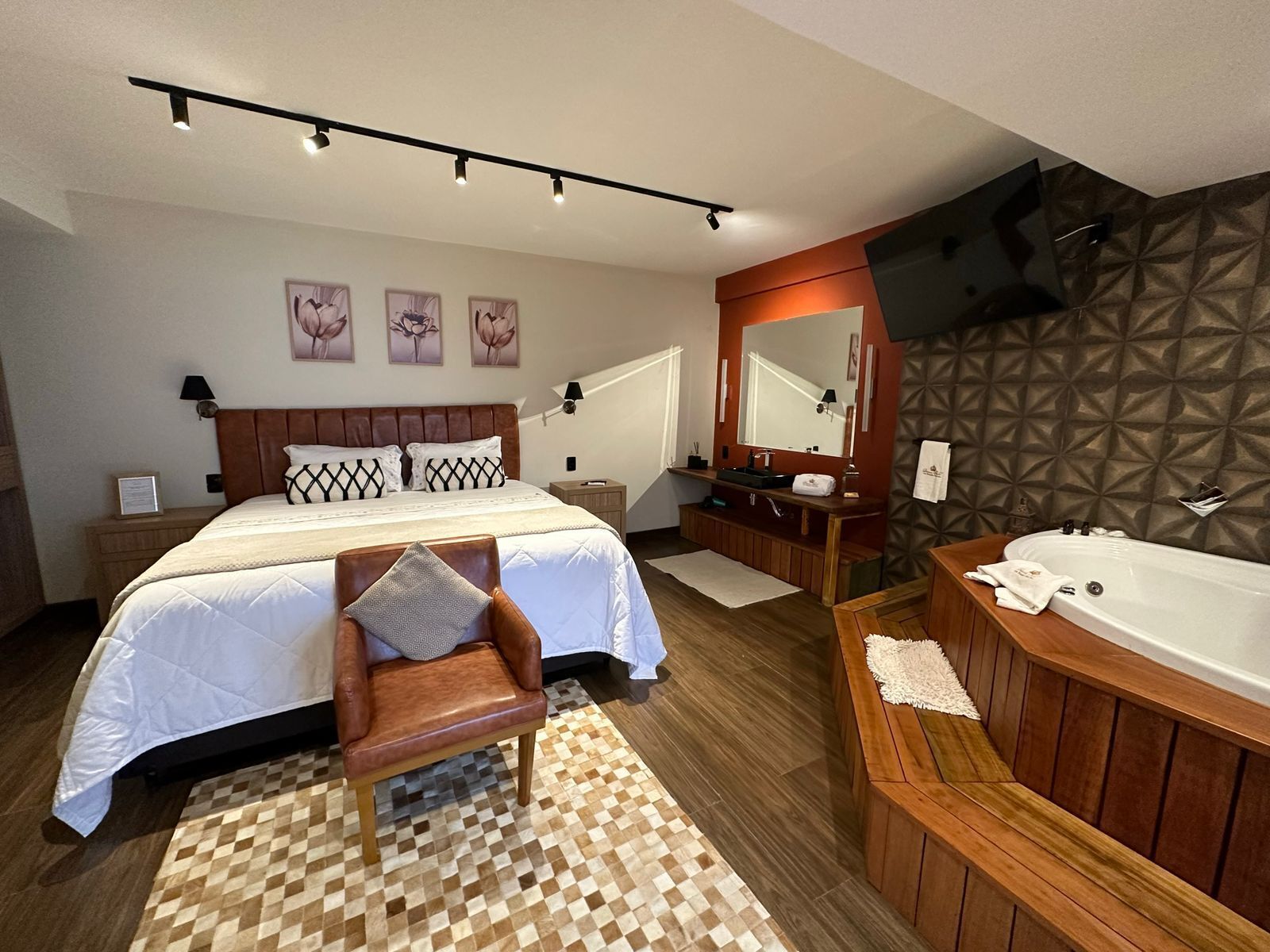 A modern hotel room with a large bed, a wooden chair, a bathroom with a bathtub, and a patterned wall.