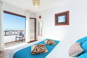 A hotel room with a balcony, a bed with blue and white bedding, and a view of the sea.