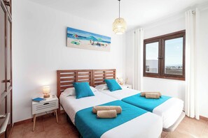 Habitación de hotel con dos camas, un cuadro de una playa, una ventana con vistas y una lámpara de noche.