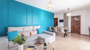 Un salon comprenant un canapé d’angle, une table basse avec une bouteille et des verres, et un coin repas avec des chaises et une table.