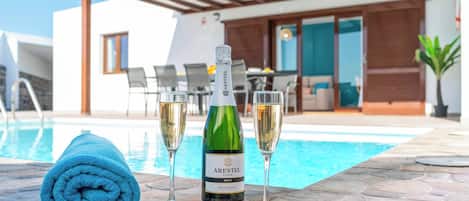 Escena junto a la piscina con una botella de Cava Brut Arestel, dos copas y una toalla azul.