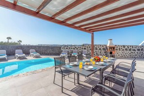A poolside area with a table set for dining, lounge chairs, and a stone wall backdrop.