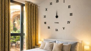A spacious bedroom with a large bed, a clock on the wall, and a view of the outdoors through a window. - Apartment "Romantik" - an apartment with a special character (Mürlenbach)