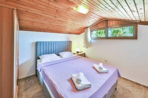 A bedroom with a wooden ceiling, a bed with a blue headboard, a window with a view of greenery, and a nightstand with a lamp. - Villa Beste - Four Bedroom Villa, Sleeps 7 (Dalyan)