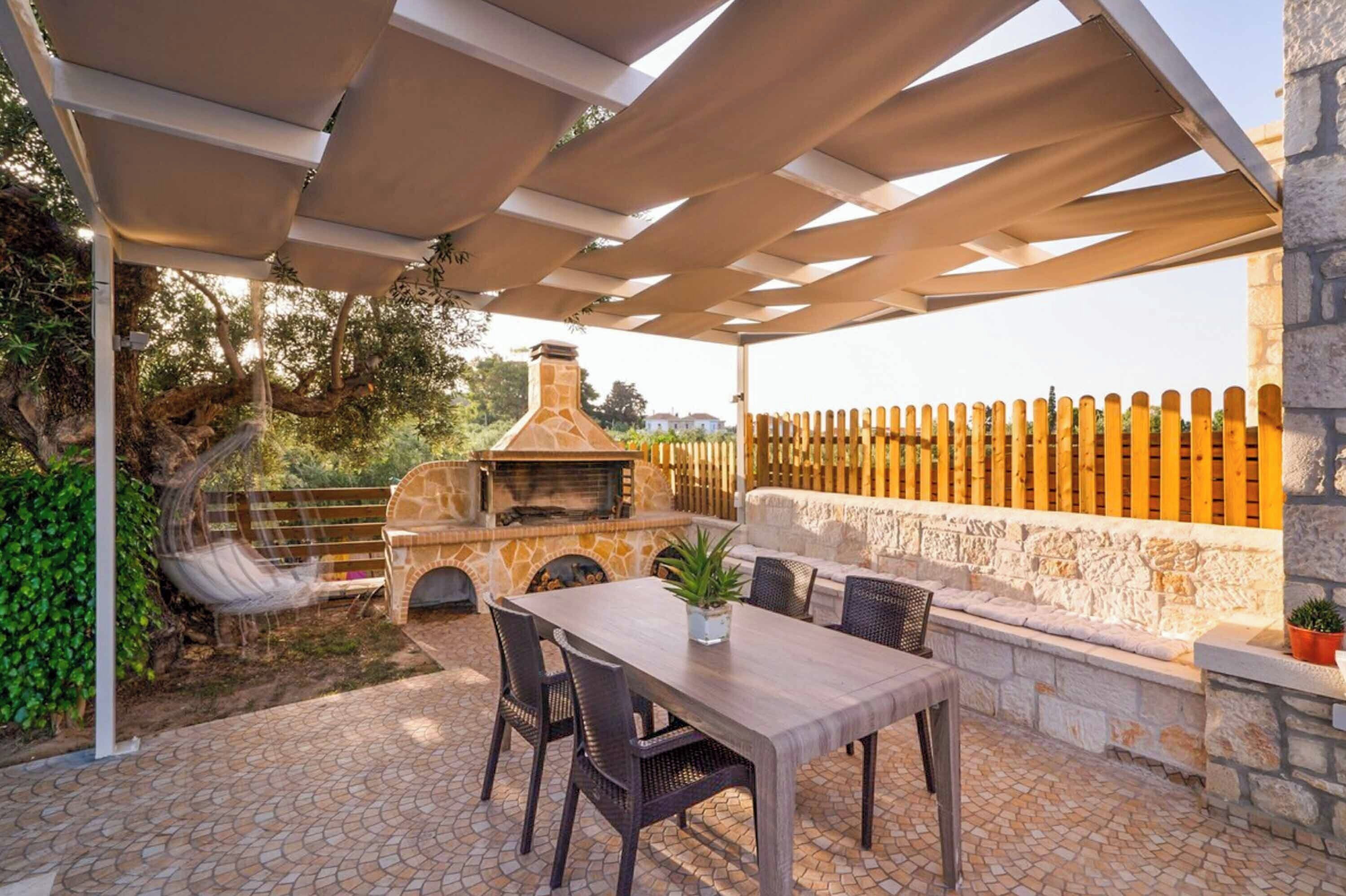 An outdoor patio with a stone fireplace, a wooden table, and chairs.