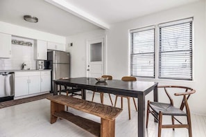 Una cocina con armarios blancos, un refrigerador de acero inoxidable, una mesa de comedor con sillas y un banco.