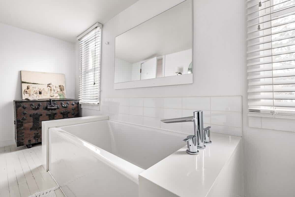 Een moderne badkamer met een witte badkuip, een grote spiegel en een houten dressoir.