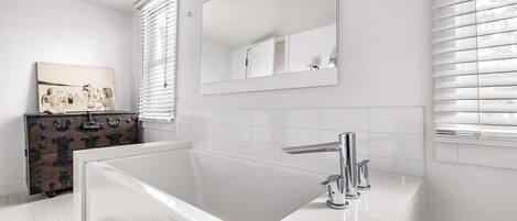 Een moderne badkamer met een witte badkuip, een grote spiegel en een houten dressoir.