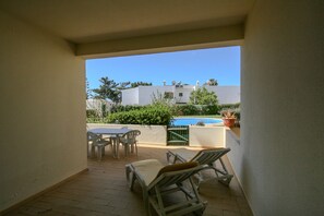 A patio with a table and chairs, a pool, and a view of buildings in the background.