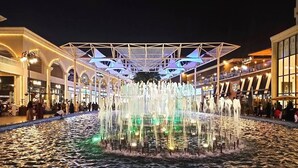 Eine beleuchtete Springbrunnenanlage mit Wasserstrahlen, umgeben von einem überdachten Gang und stimmungsvoller Beleuchtung.