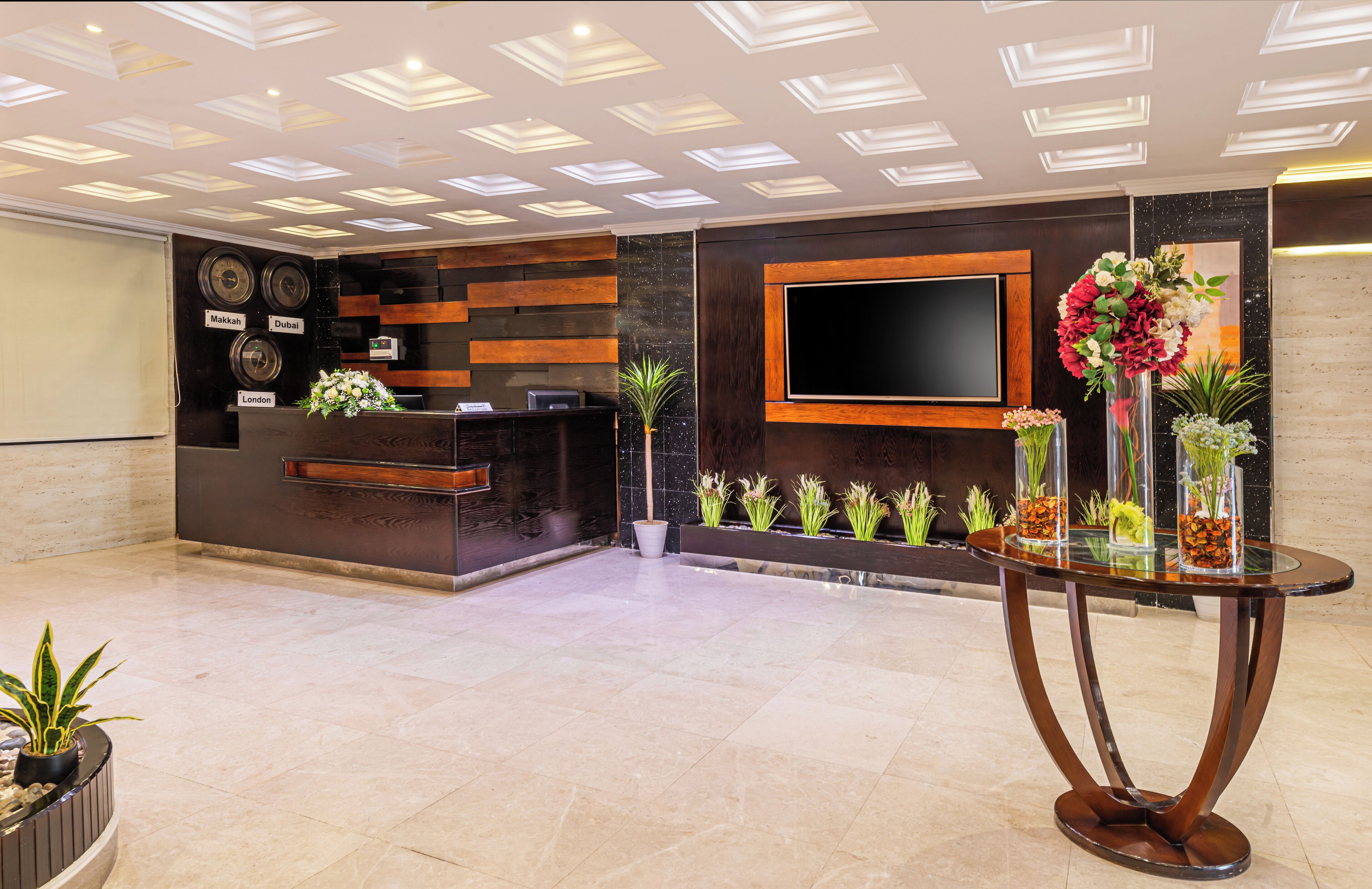 A reception area with a modern design, featuring a reception desk, a flat-screen TV, and decorative plants.