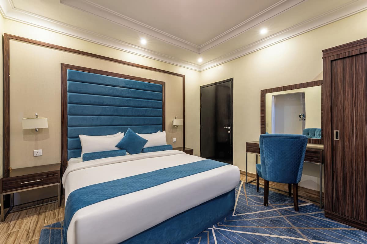 A hotel room with a large bed, a desk, a chair, and a wardrobe.