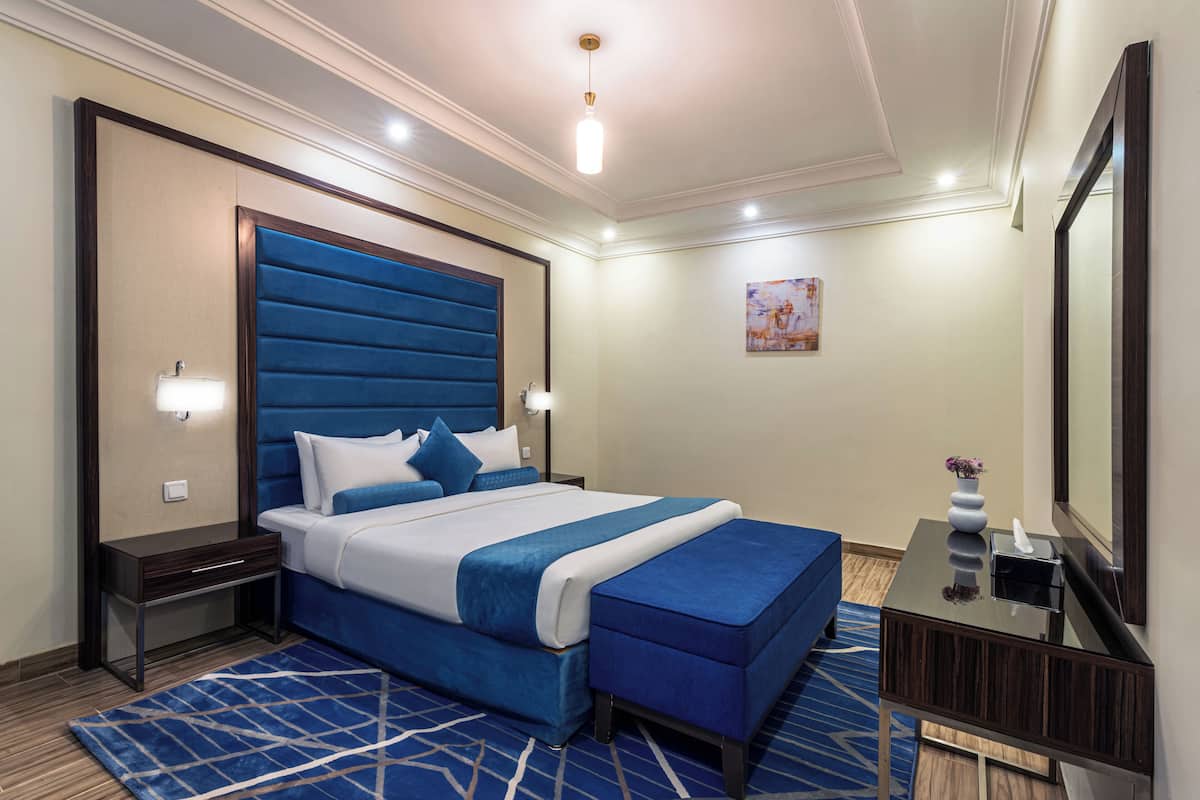 A modern hotel room with a large bed, a bedside table, a nightstand, a dresser, a mirror, and a blue accent wall.