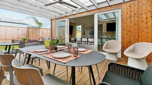 An outdoor patio with a round table set for dining, surrounded by chairs, and a ceiling fan overhead.