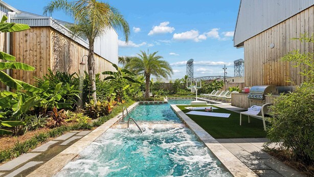 A swimming pool with a waterfall feature, surrounded by lush greenery and a barbecue area.