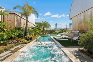 Una piscina con cascada, rodeada de exuberante vegetación y una zona de barbacoa.
