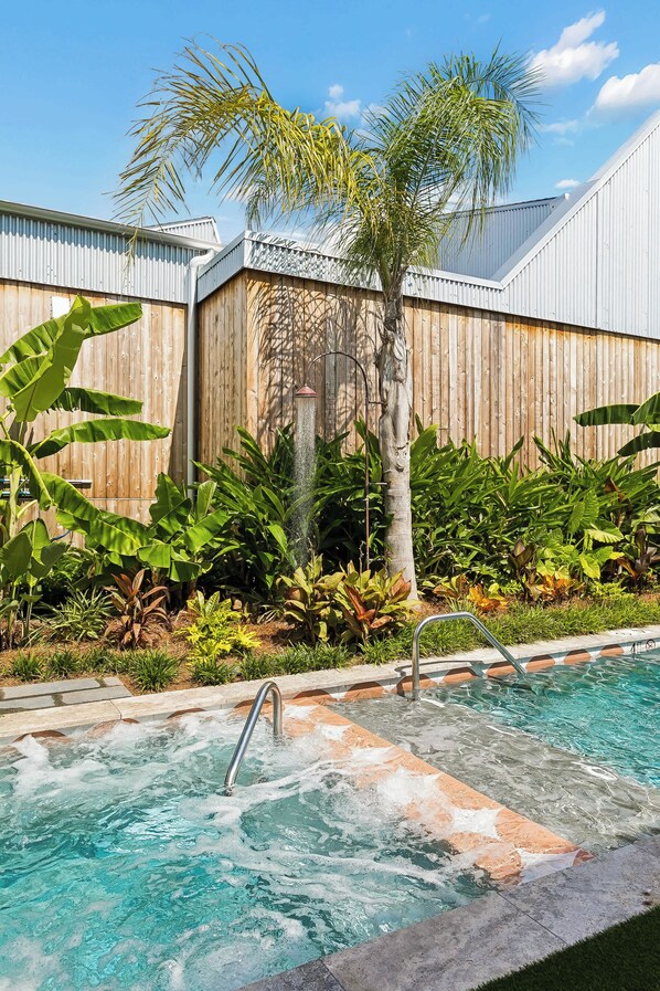 Una piscina con una escalera de metal, rodeada de exuberante vegetación tropical y una valla de madera.