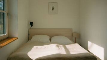Un dormitorio con cama, ventana, lámpara de noche y un cuadro en la pared.