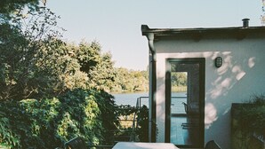 Un patio con una mesa y sillas, una puerta que da a una piscina y abundante vegetación alrededor.