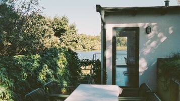 Un patio con una mesa y sillas, una puerta que da a una piscina y abundante vegetación alrededor.