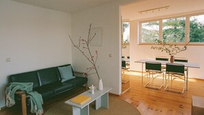 Una sala de estar moderna con un sofá verde, una pequeña mesa blanca con un jarrón y un comedor con una mesa blanca y sillas verdes.
