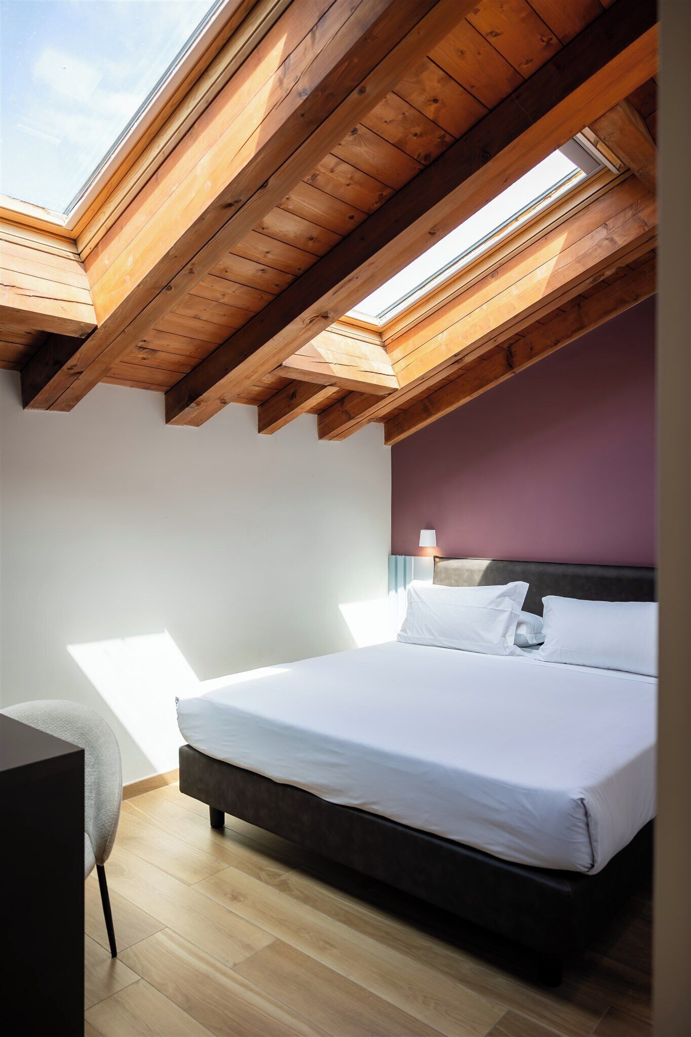 A bedroom with a skylight, a bed, a desk, and a chair.