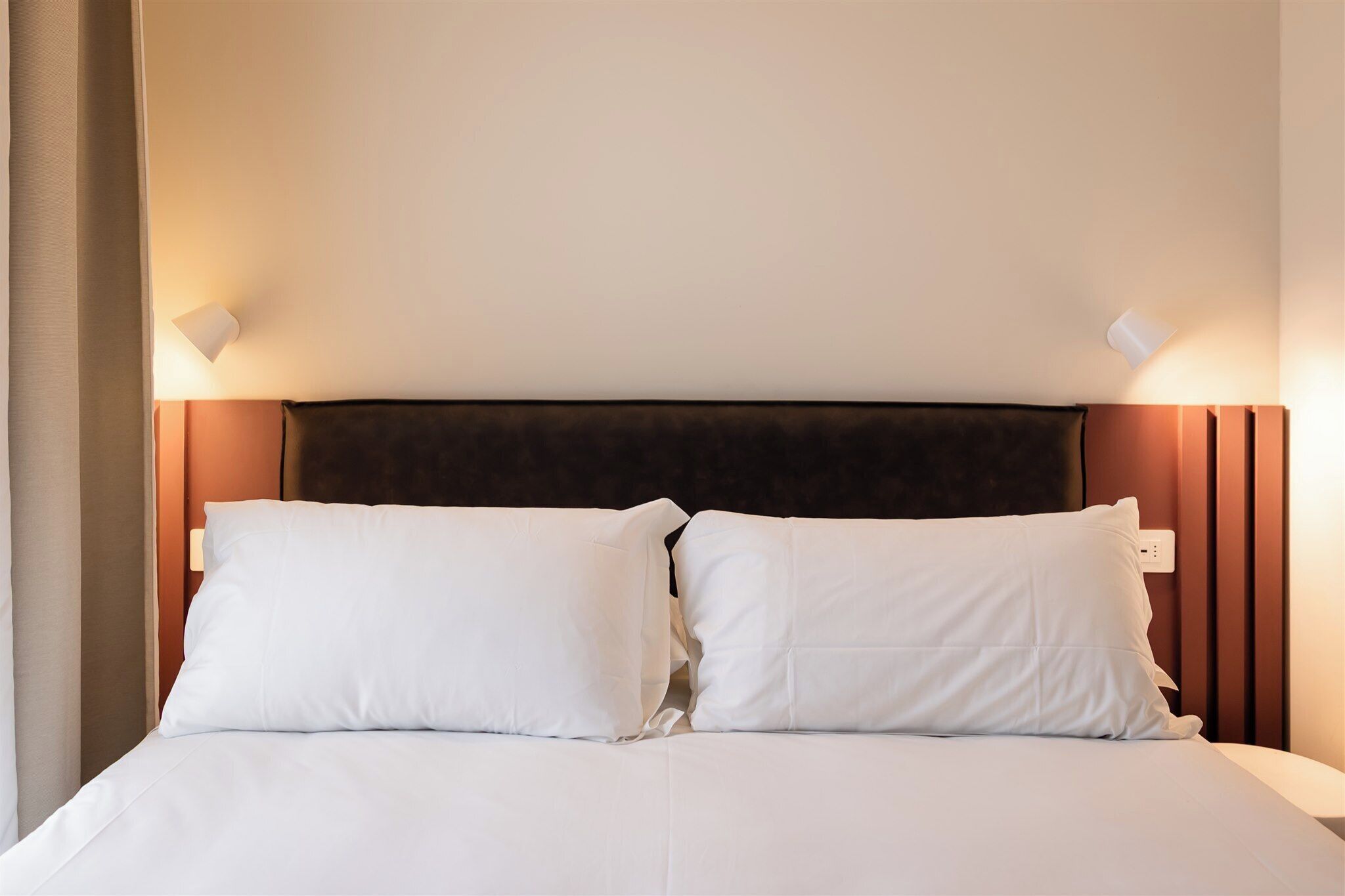 A bed with white bedding, a dark headboard, and two wall-mounted light fixtures.